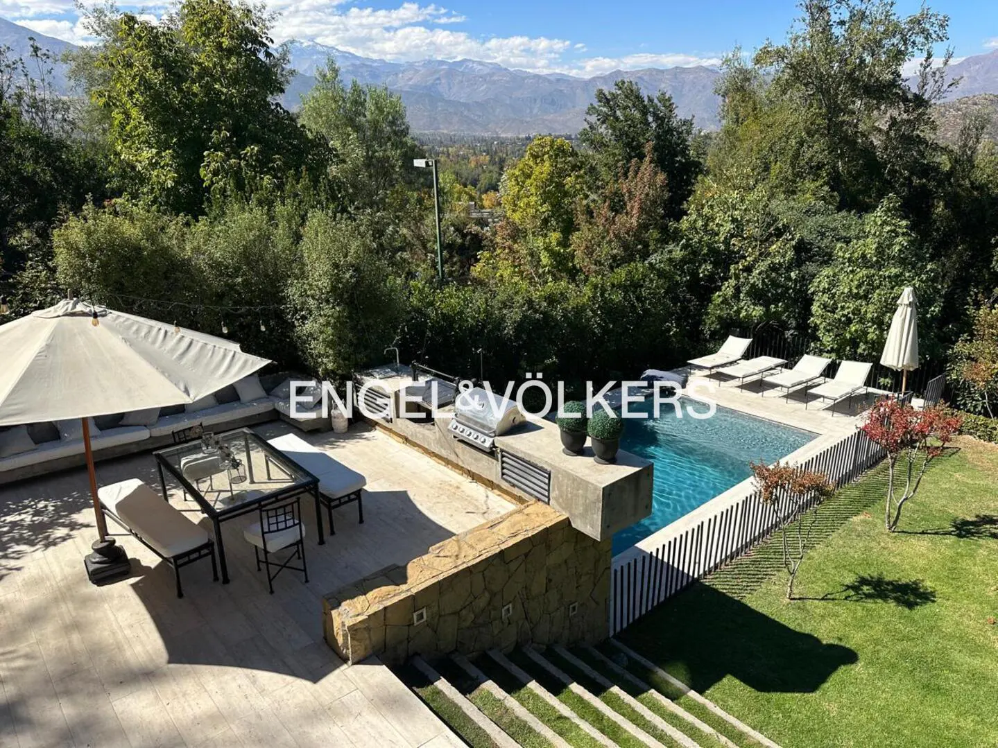 Aerial view of a backyard with a pool, lounge chairs, dining area, grill, and mountain views.