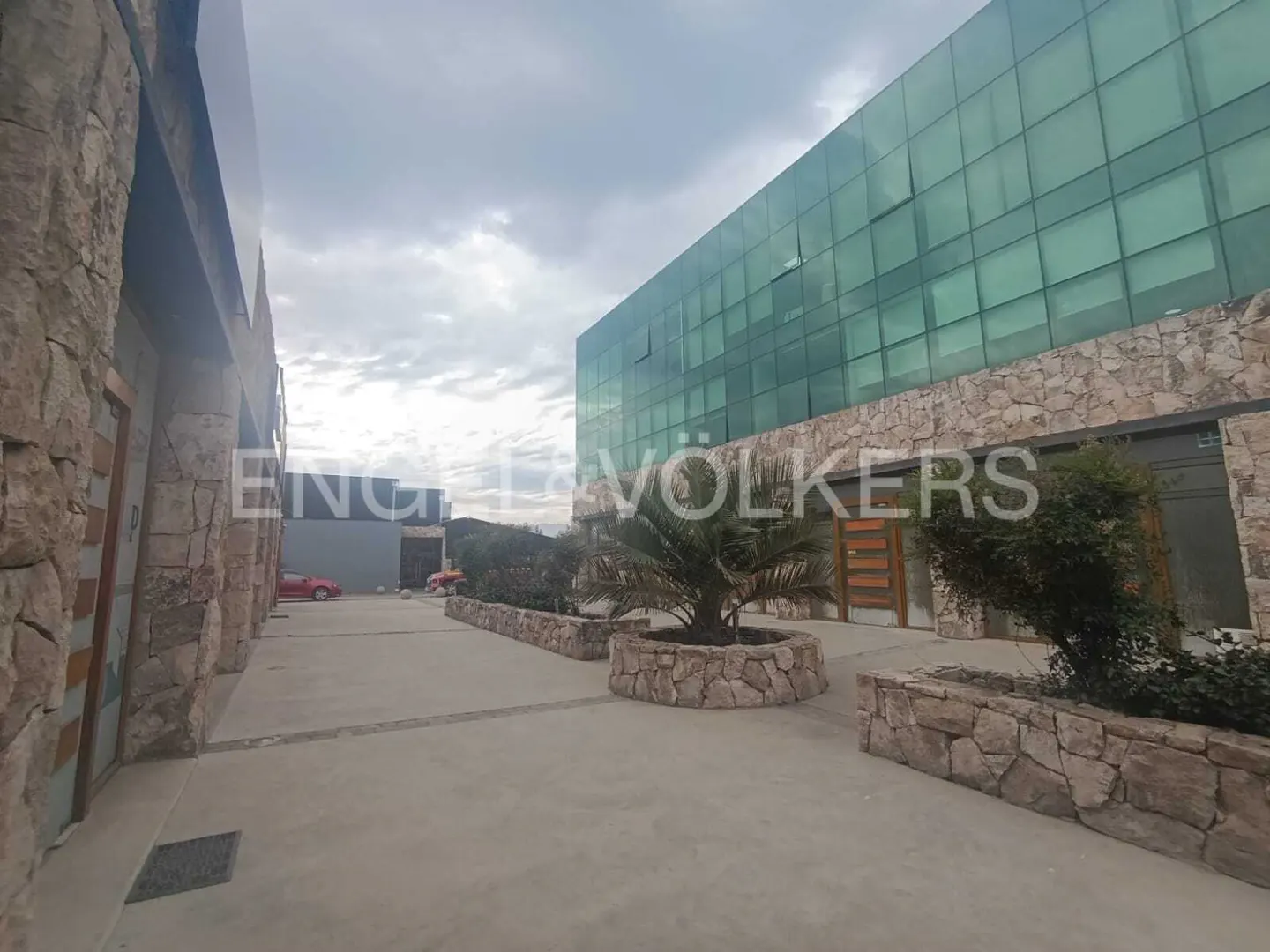 Exterior view of a modern building with glass windows and stone accents, featuring landscaping and the Engel & Volkers logo.