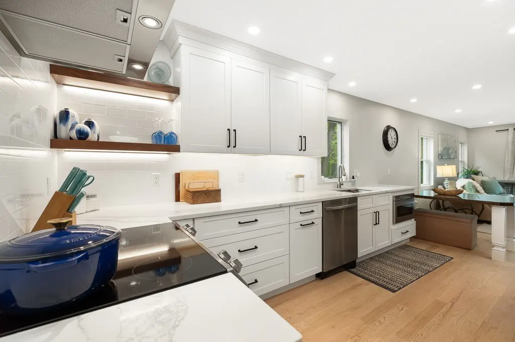 Bright, modern kitchen with white cabinets, marble countertops, and stainless steel appliances. A blue pot sits on the black stovetop.