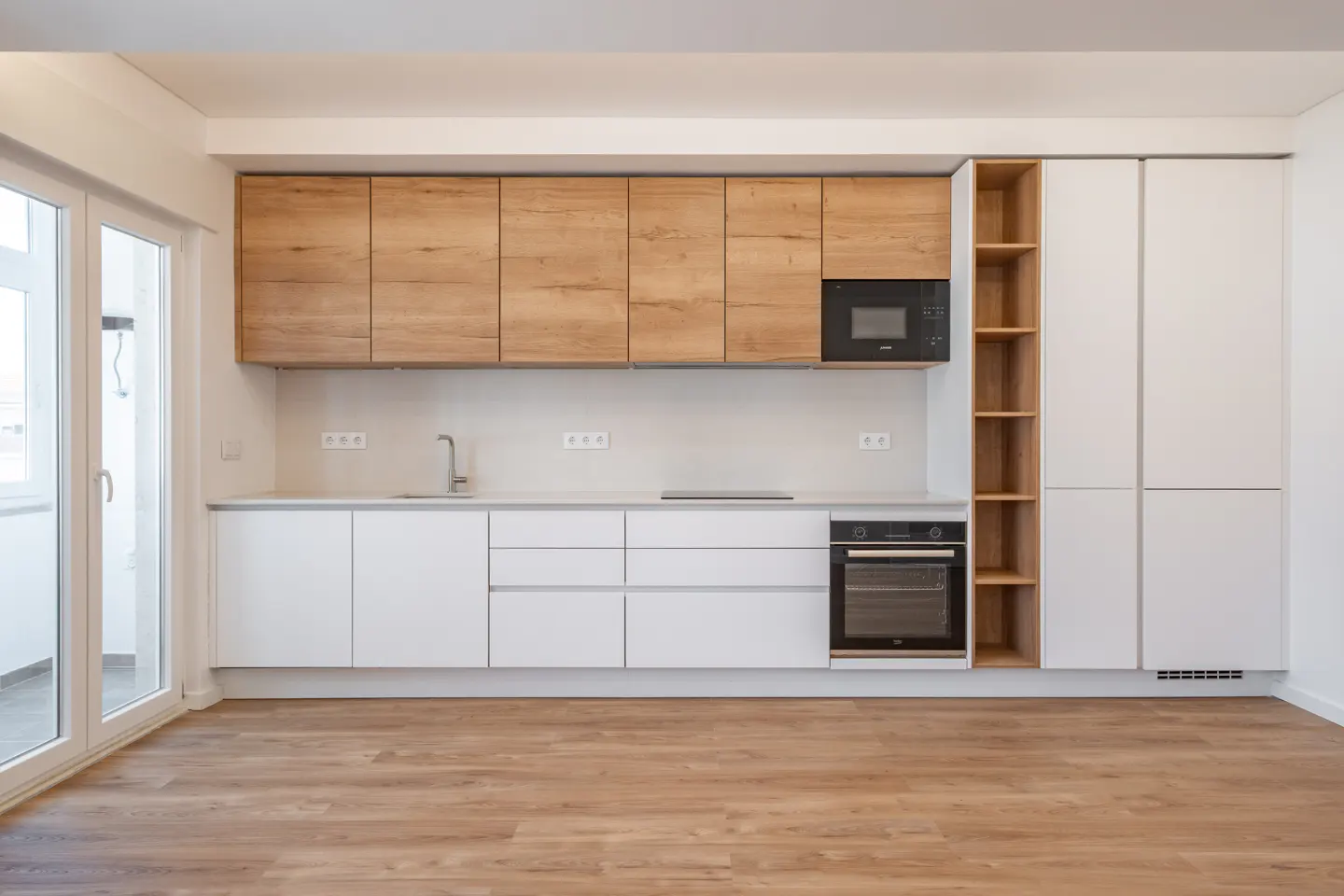 A modern kitchen with light wood floors, white lower cabinets, and wood-grain upper cabinets. A black microwave and oven are built-in.