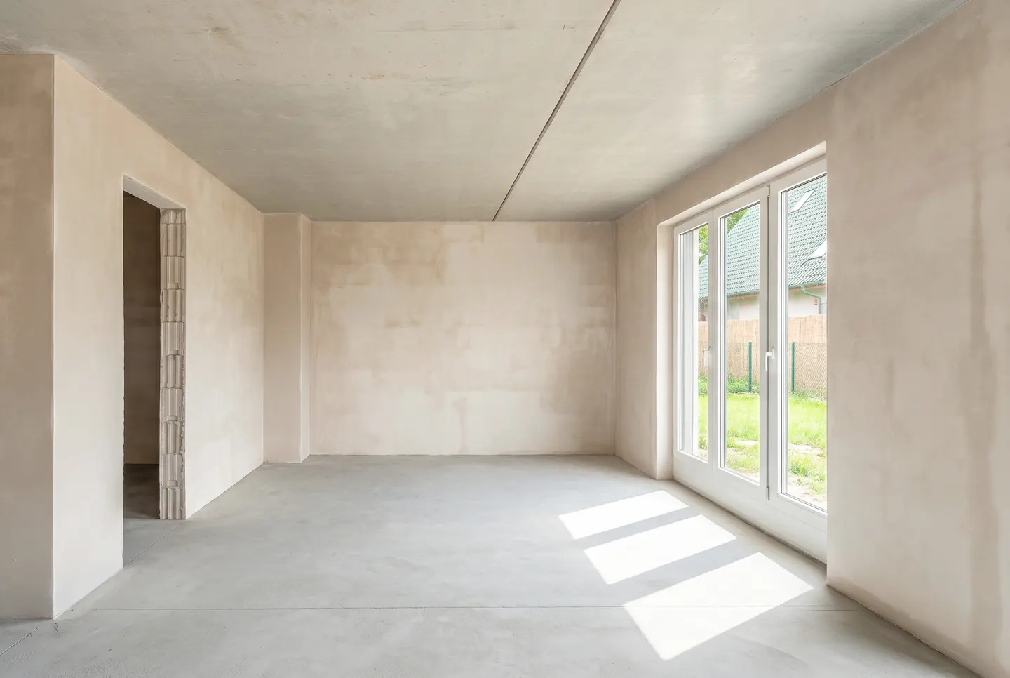 Unfinished room with concrete floor and walls, white window with view of green lawn.