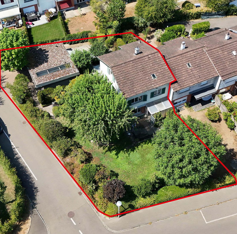 Aerial view of a house with a large green yard and mature trees, outlined in red, situated on a corner street lot. [AI-generated text]