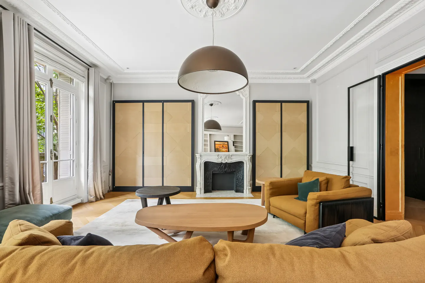 Elegant living room with a fireplace, large dome pendant light, mustard sofas, and tall beige cabinets on a wood floor.