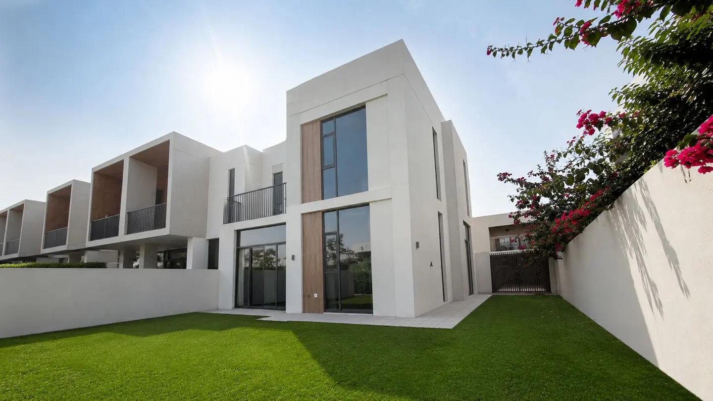 Modern two-story white house with large windows and a green lawn. Bougainvillea flowers grow along the white wall.