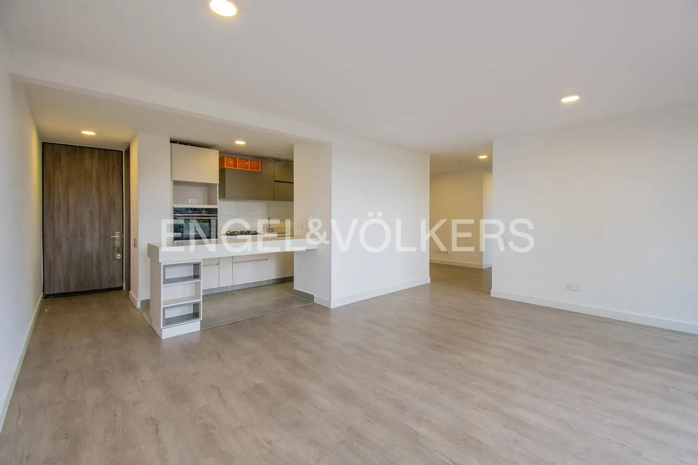 A bright, modern apartment interior with a kitchen bar, light wood floors, and white walls.