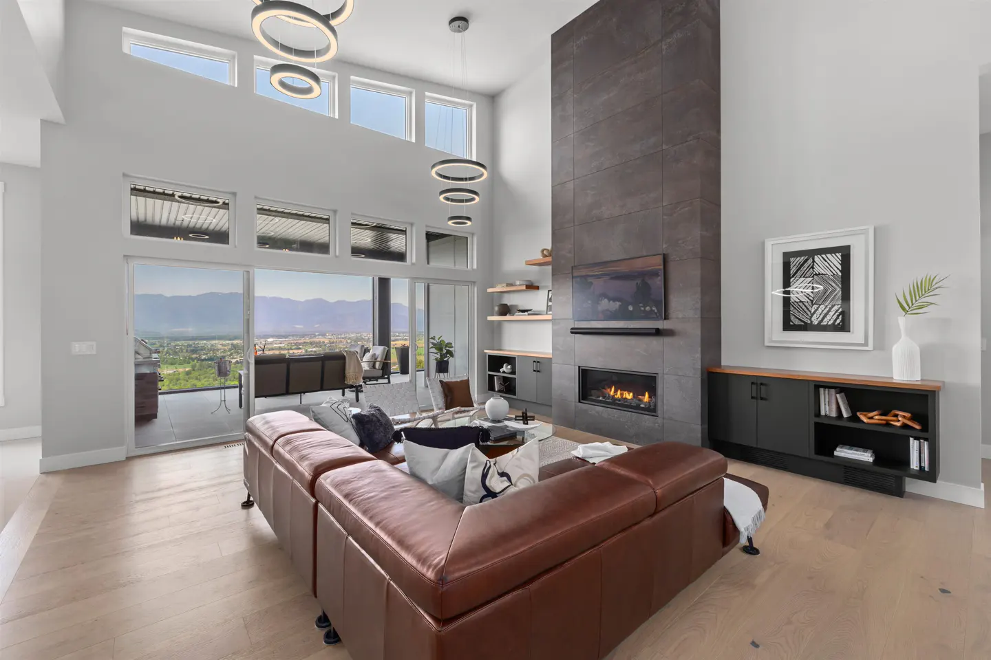 Bright living room with a brown leather sectional, fireplace, and mountain view through large windows.