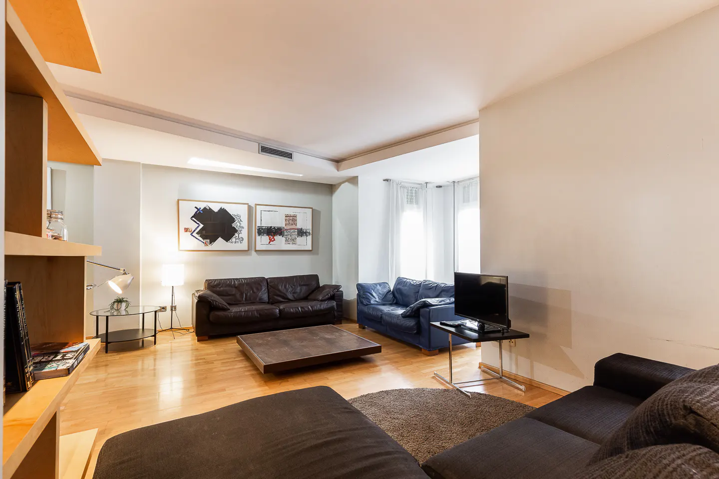 Living room with hardwood floors, brown and blue sofas, square coffee table, and abstract art on the wall.