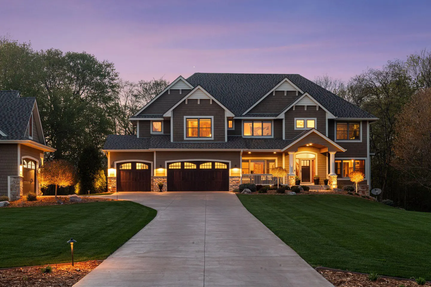 Two-story brown house with a gray roof, a driveway, and a green lawn at dusk.