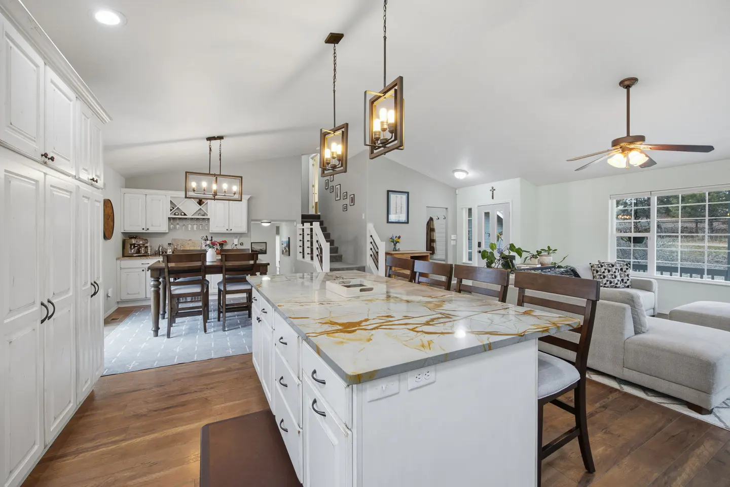 Open-concept kitchen and living room with white cabinets, a large island with gold veining, and hardwood floors.