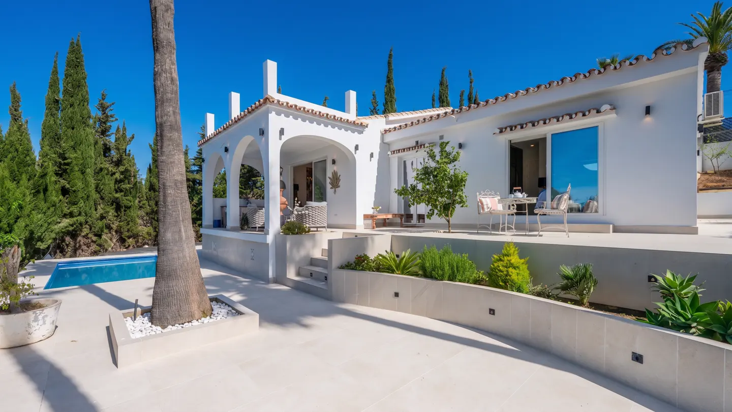 Exterior view of a white villa with a pool, patio, and garden under a clear blue sky.