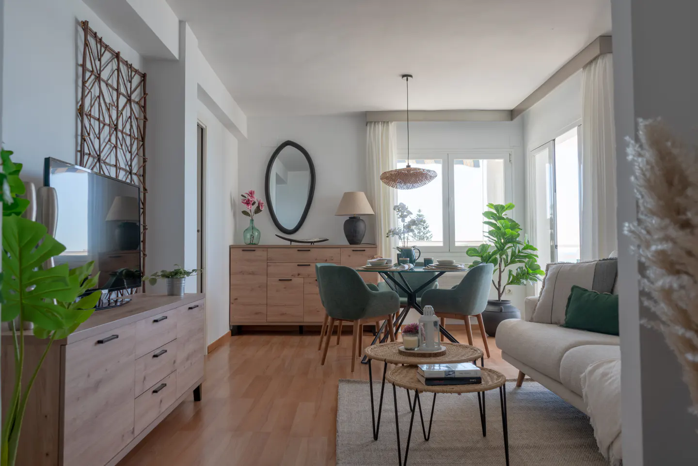 Bright living room with wood floors, white walls, and a dining area. A TV sits on a wooden cabinet next to a decorative wall hanging.