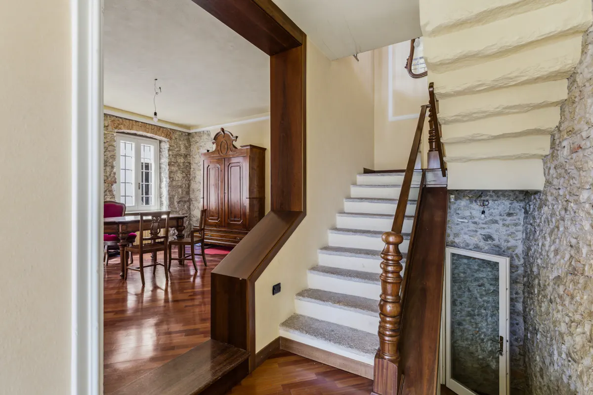 Interior view of a home featuring a wooden staircase with white steps, stone walls, and a dining room with wooden furniture.