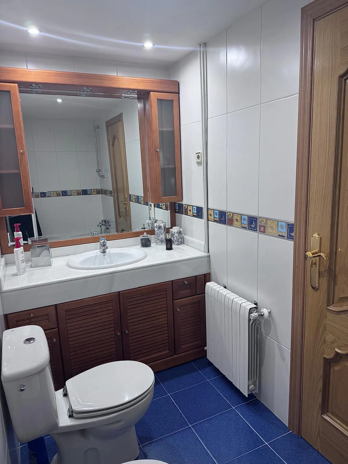 A bathroom with blue tile floors, white walls, a white toilet, and a wooden vanity with a white countertop.