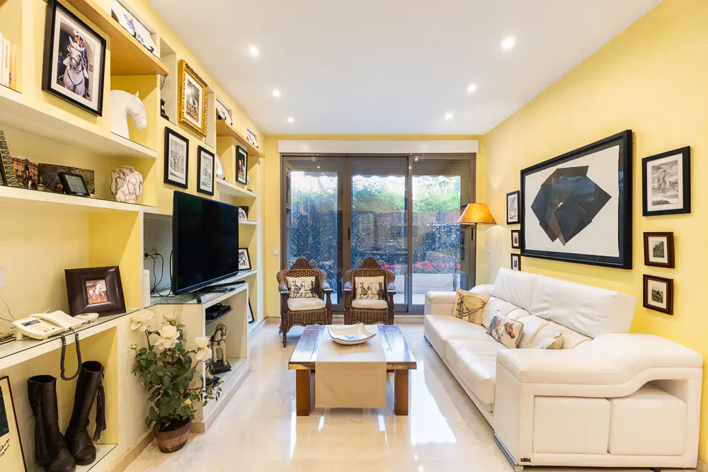 Bright living room with yellow walls, white sofa, and built-in shelves filled with decor. Sliding glass doors lead to a garden.