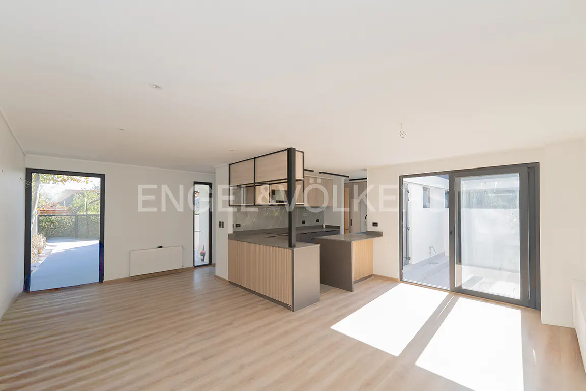 Bright, modern open-plan living space with light wood floors, a kitchen island, and sliding glass doors to an outdoor area.