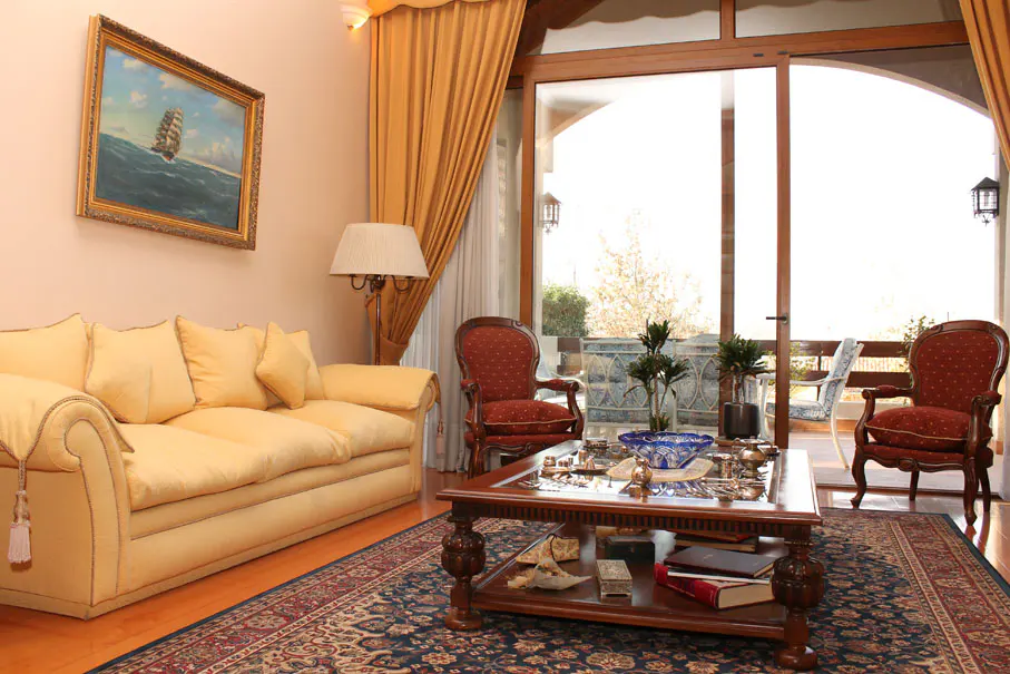 Living room with yellow sofa, red chairs, and a dark wood coffee table on a blue patterned rug. A painting of a ship hangs above the sofa.