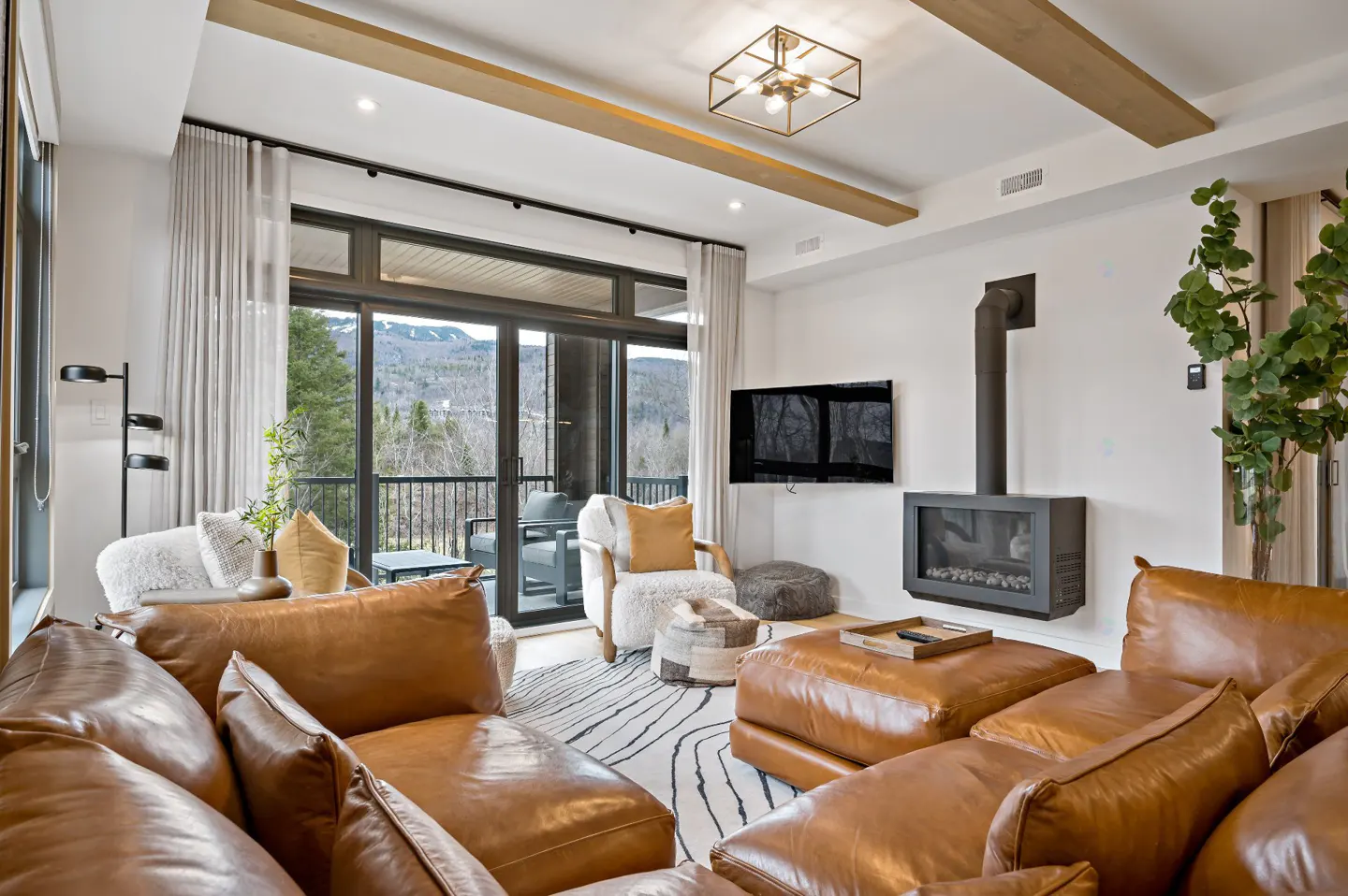 Living room with a brown leather sectional, fireplace, TV, and a view of mountains through sliding glass doors.