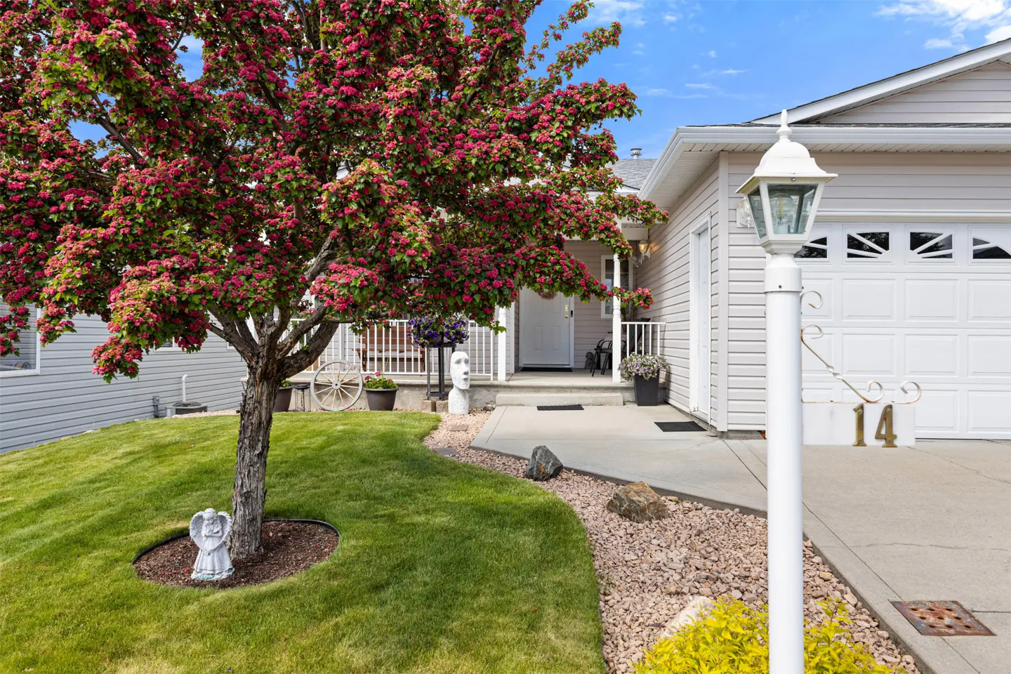A beige house with a white garage door and a blooming pink tree in the front yard. A white lamp post stands near the driveway.
