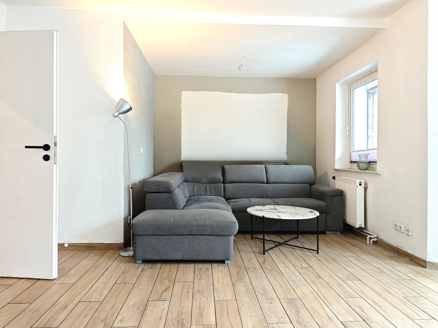 Living room with gray sectional sofa, marble table, wood floors, and a white door. A silver floor lamp stands near the sofa.
