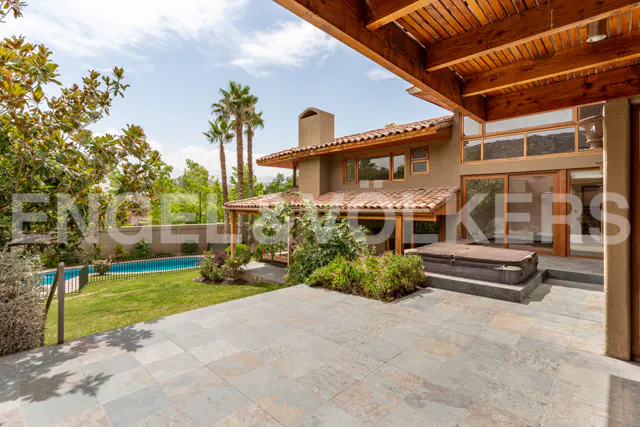 Stone patio overlooking a backyard with a swimming pool, hot tub, and palm trees under a wooden pergola.