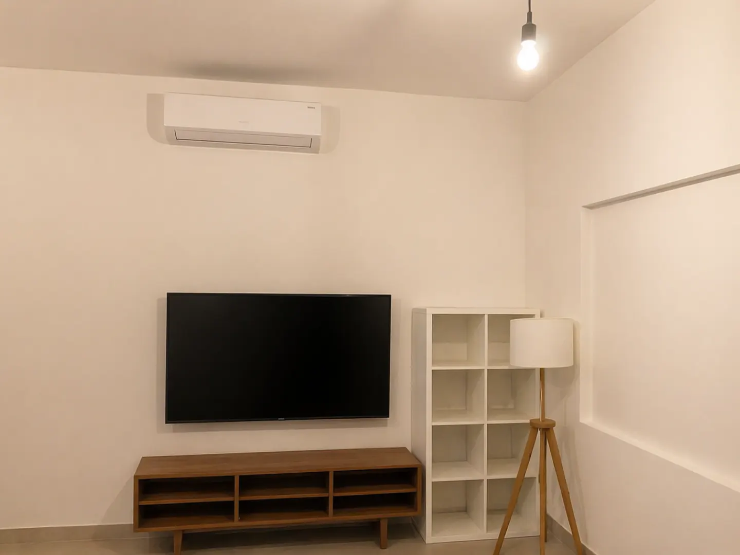 A living room with white walls, a black TV, a brown TV stand, a white bookshelf, and a floor lamp.