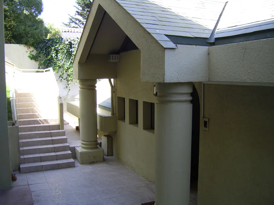 Exterior view of a building with columns, a tiled roof, and stairs leading up to a higher level.