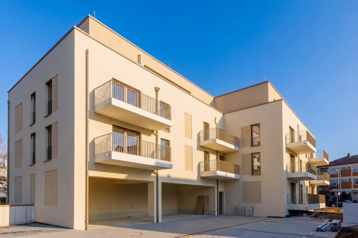 Modern apartment building with beige facade, balconies, and garage parking under a clear blue sky.