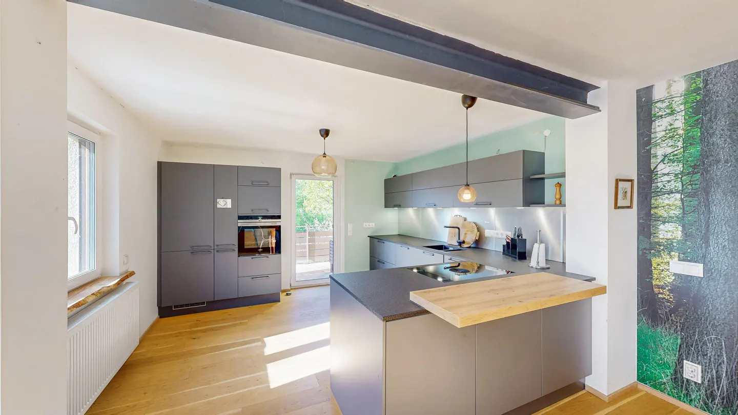 A modern kitchen with gray cabinets, wood floors, and a central island with a light wood countertop. A forest mural adorns a wall.