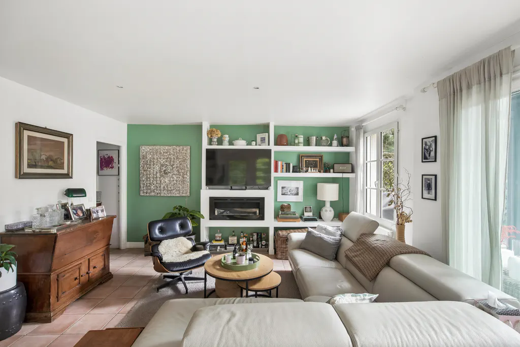 Living room with white sofa, black chair, and green accent wall with built-in shelves and a TV above a fireplace.