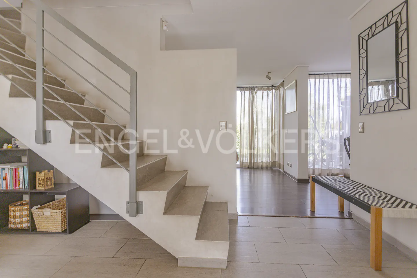Entryway with a staircase, light beige tile floor, and a bench. The stairs have a gray metal railing. A mirror hangs on the wall.