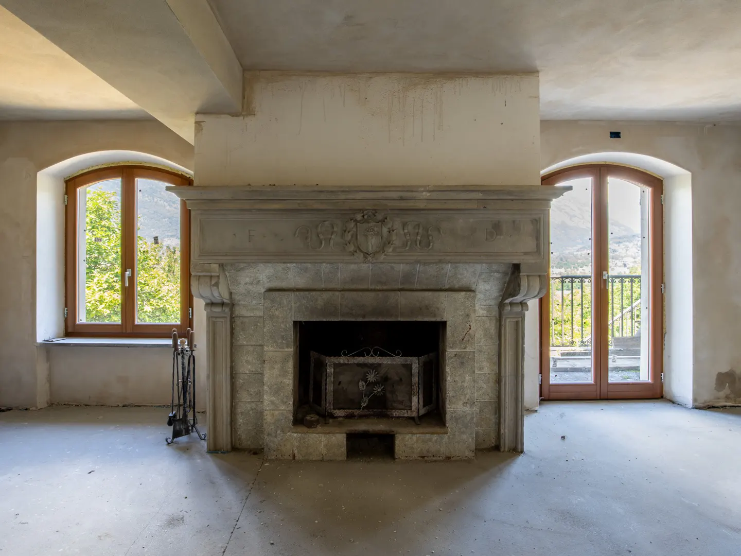 Unfinished room with a stone fireplace, arched windows, and a view of greenery.