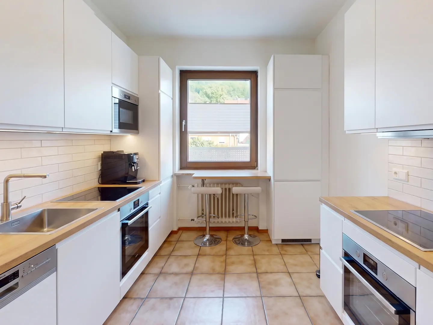 Modern galley kitchen with white cabinets, light wood countertops, stainless steel appliances, and a window breakfast bar.