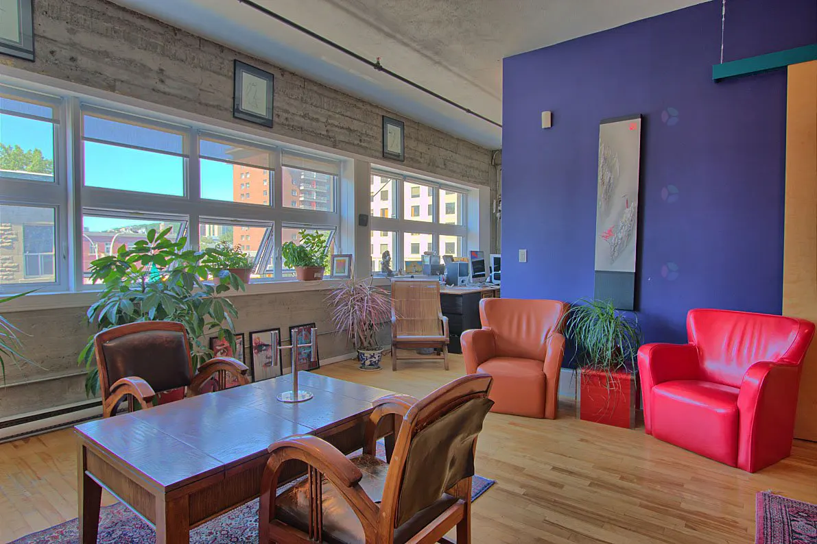 Bright, airy loft with hardwood floors, large windows, and colorful accent wall. Furnished with leather chairs, a wooden table, and potted plants.