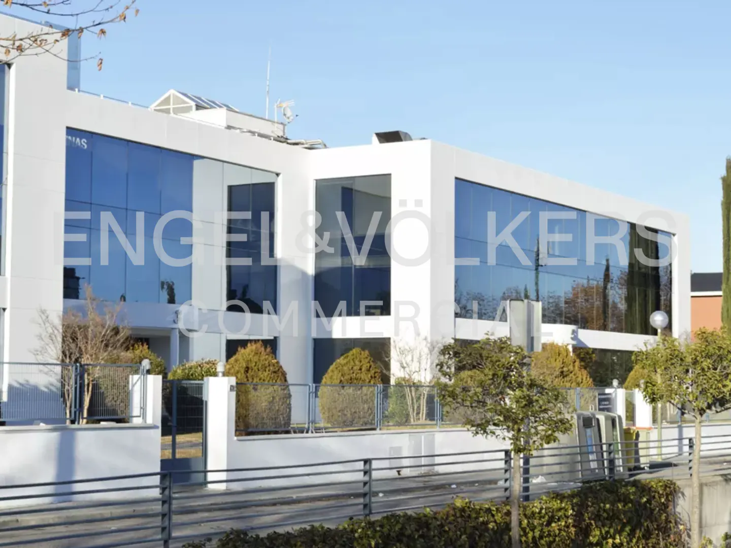 Exterior view of a modern, white Engel & Völkers commercial building with large, reflective windows on a sunny day.