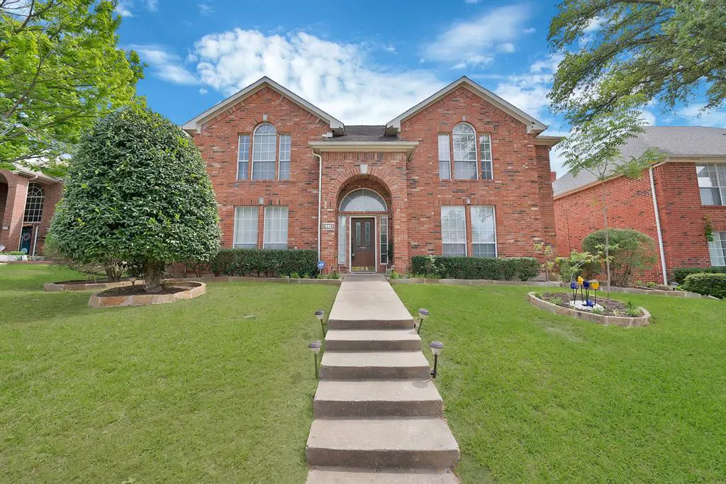 Two-story brick house with a concrete walkway leading to the front door, green lawn, and blue sky.