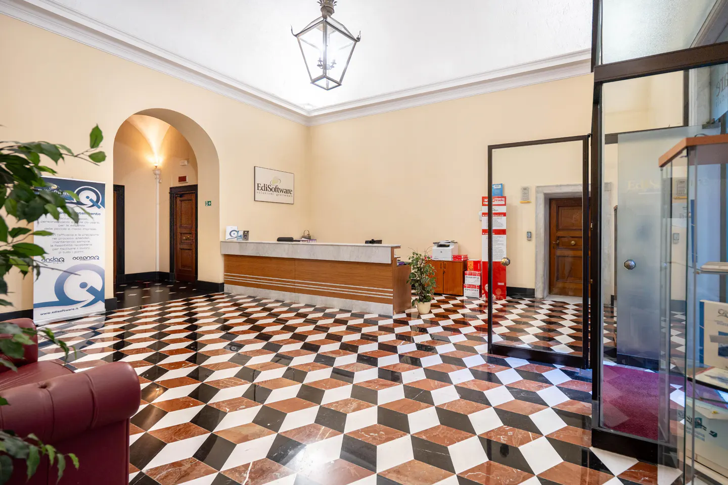 Office lobby with a reception desk, black, white, and brown geometric tile floor, and a glass door.