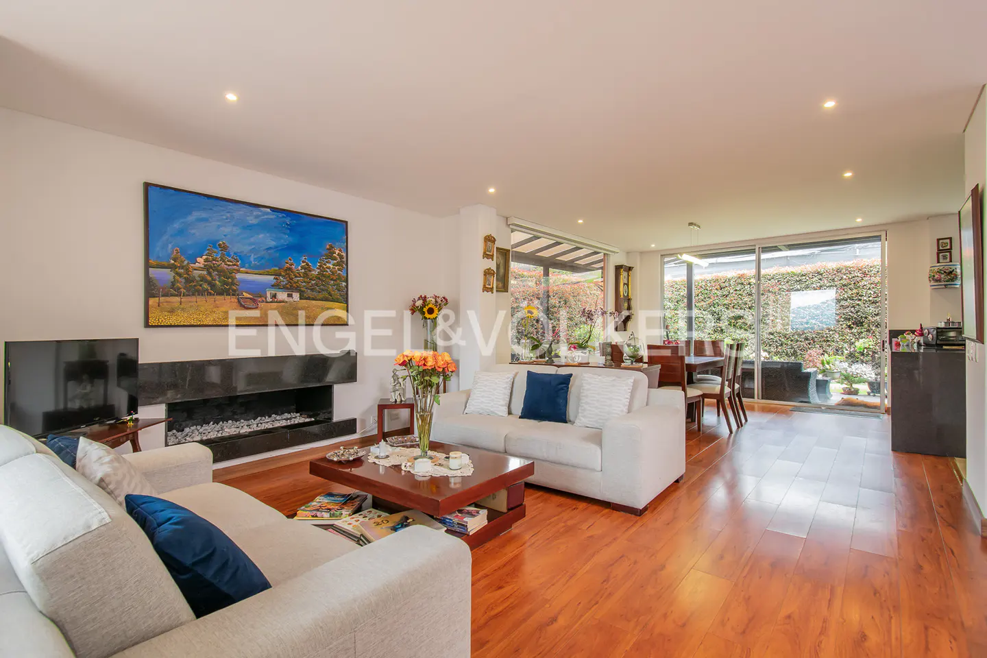 Bright living room with hardwood floors, white sofas with blue pillows, a black fireplace, and a large painting.