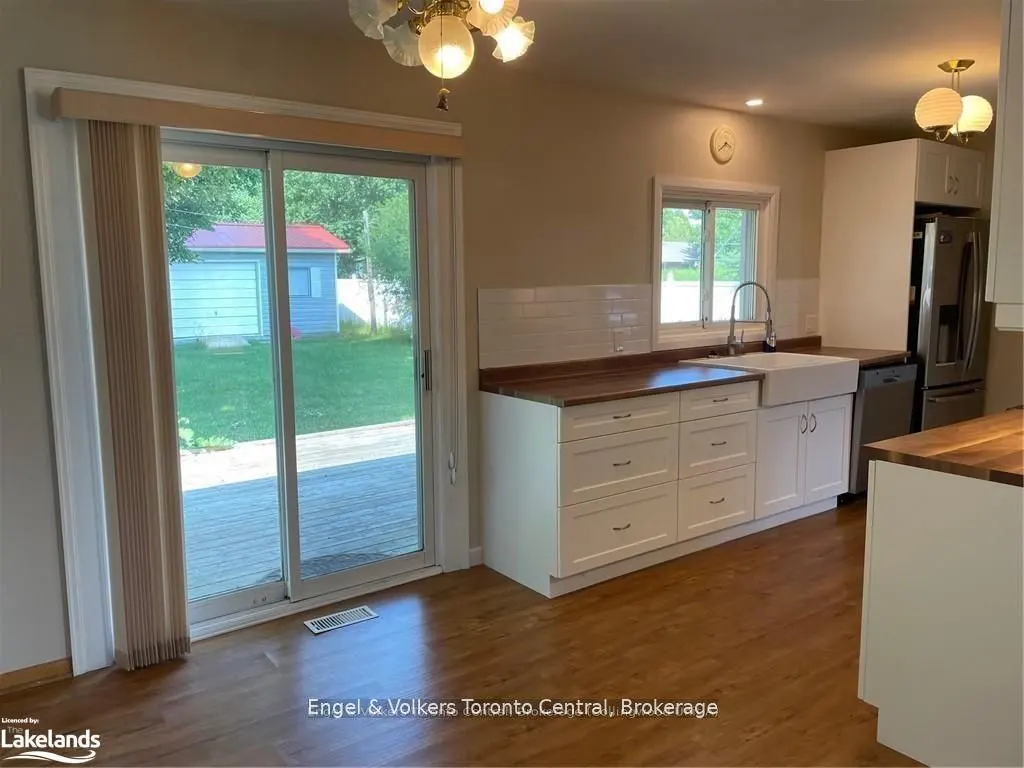 Bright kitchen with wood floors, white cabinets, and butcher block countertops. Sliding glass doors lead to a deck and backyard.