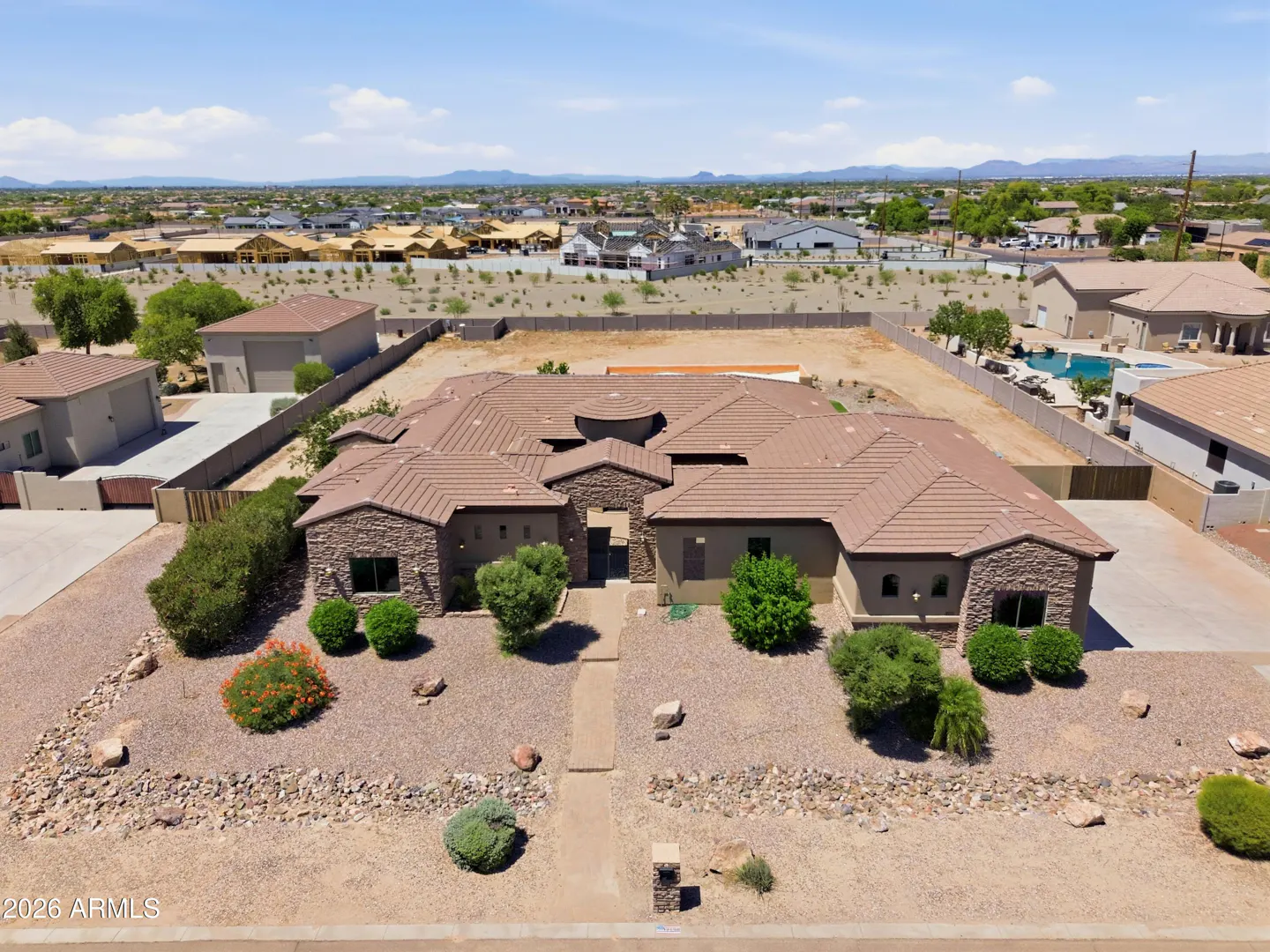 Aerial view of a tan stucco home with a brown tile roof, desert landscaping, and a surrounding suburban neighborhood.