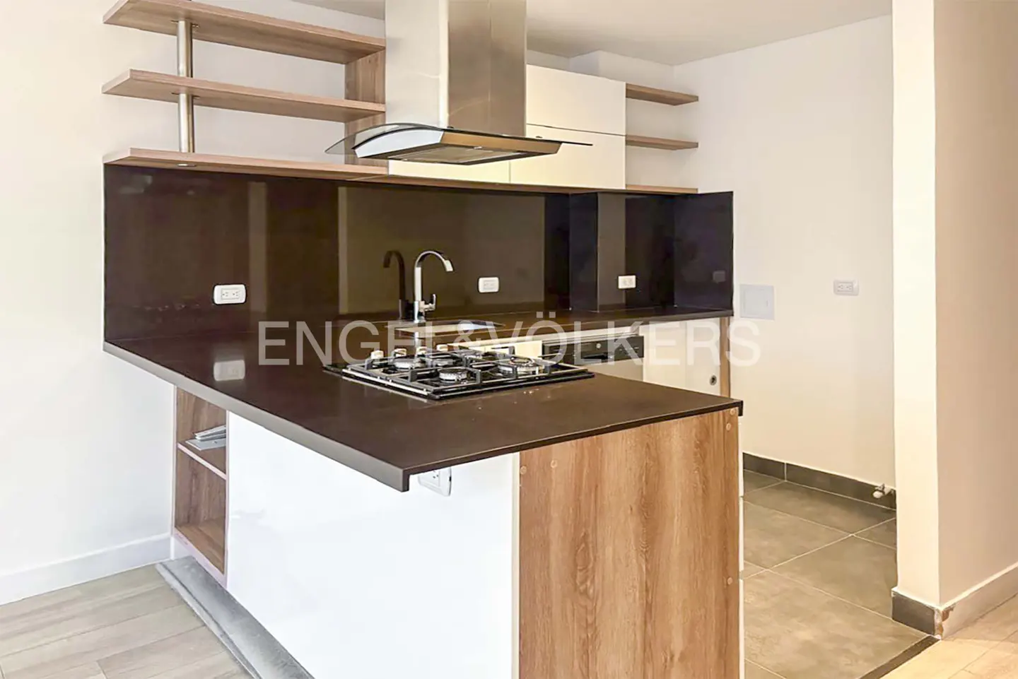 Modern kitchen with brown countertop island, gas stove, stainless steel hood, and light wood shelves.