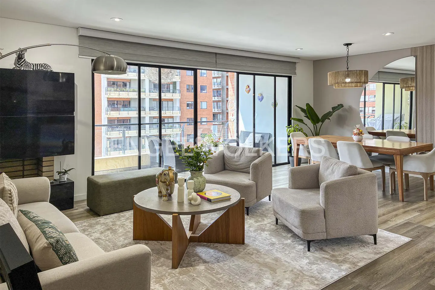 Modern living room with beige sofas, a round wooden coffee table, and a dining area with a wooden table and chairs.