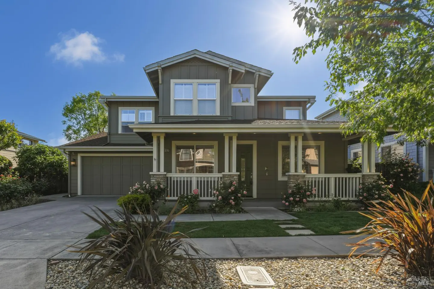 Two-story olive green house with white trim, a front porch with white railings, and a two-car garage on a sunny day.