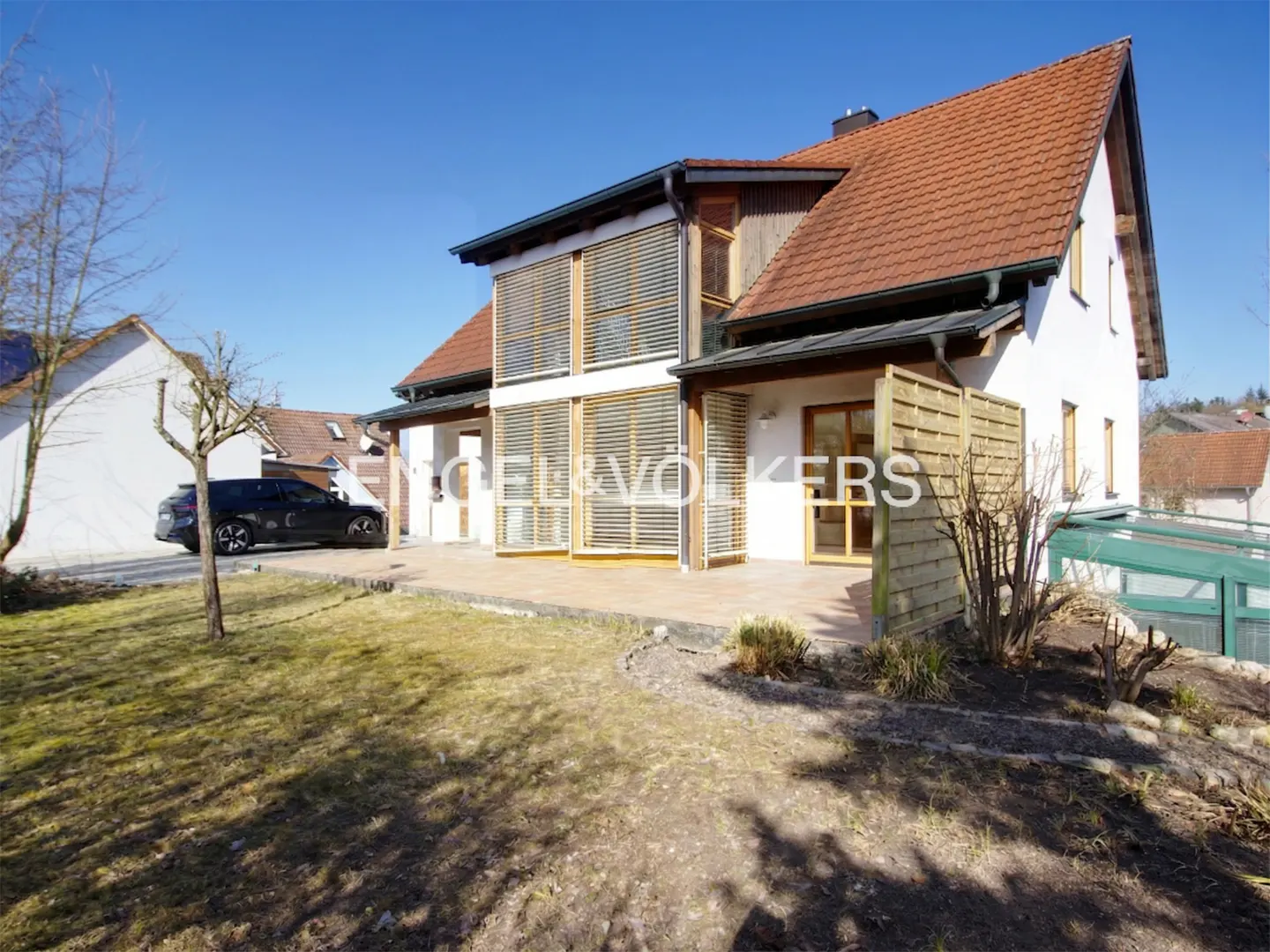 Exterior view of a two-story house with a red tile roof, white walls, and wooden shutters. A black car is parked in the driveway.