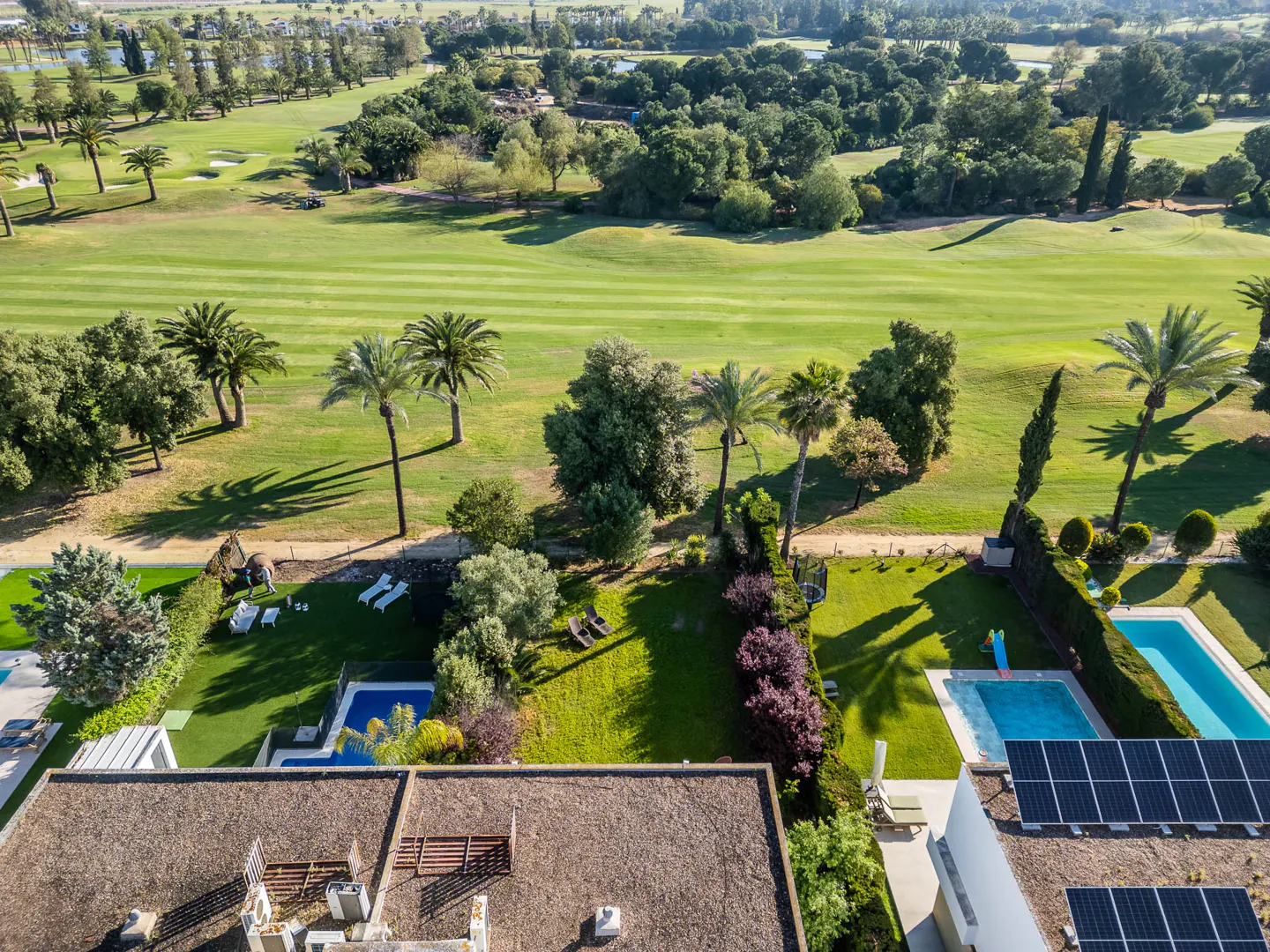 Aerial view of a property with a pool, solar panels, and a golf course in the background.