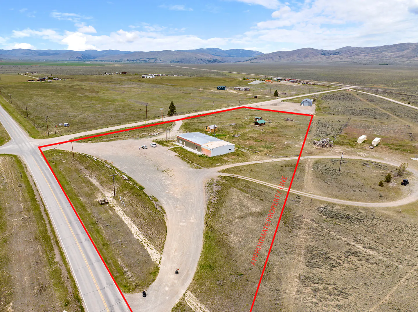 Aerial view of a rural property outlined in red, featuring a commercial building, small sheds, and gravel access roads.