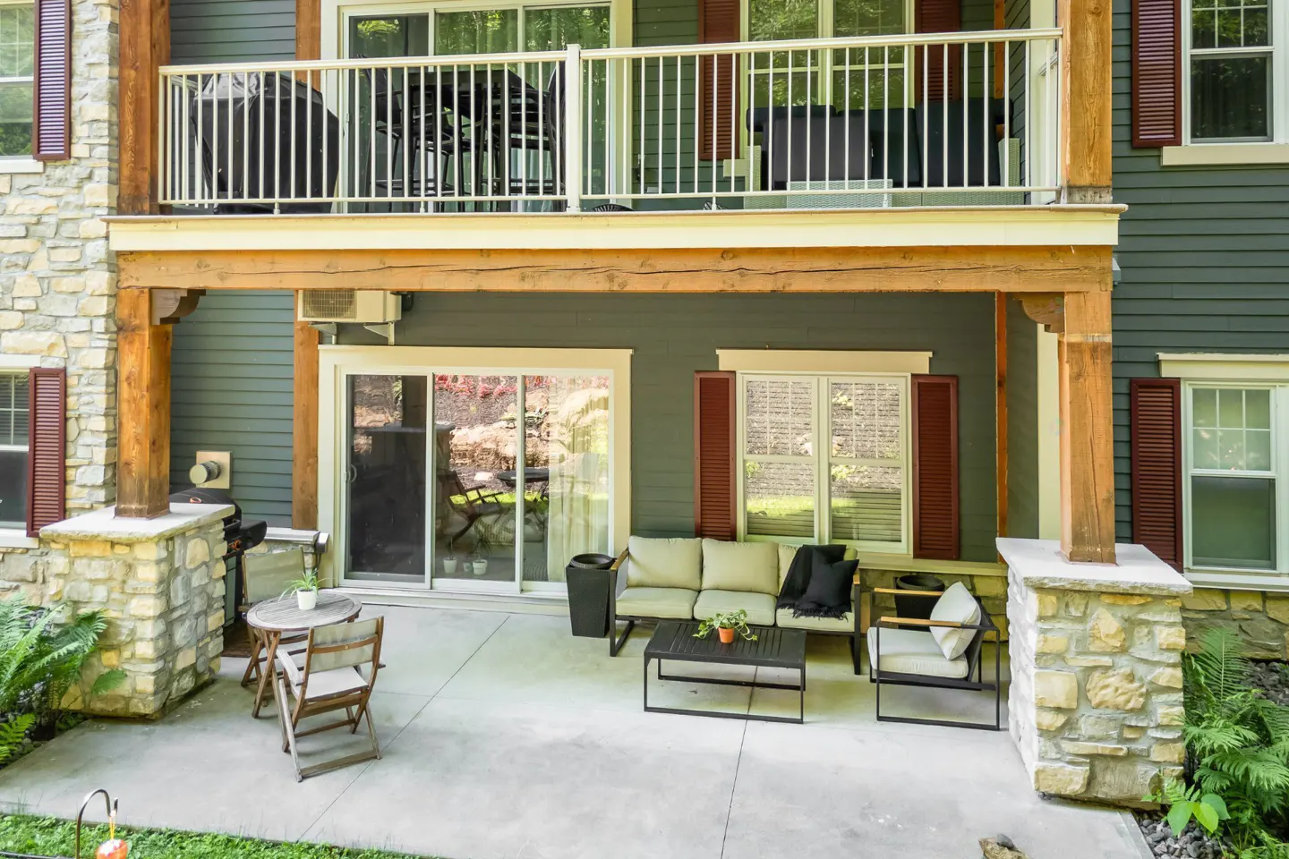Outdoor patio with furniture, including a sofa, chairs, and a table. The building has stone pillars and wood accents. A balcony is above.