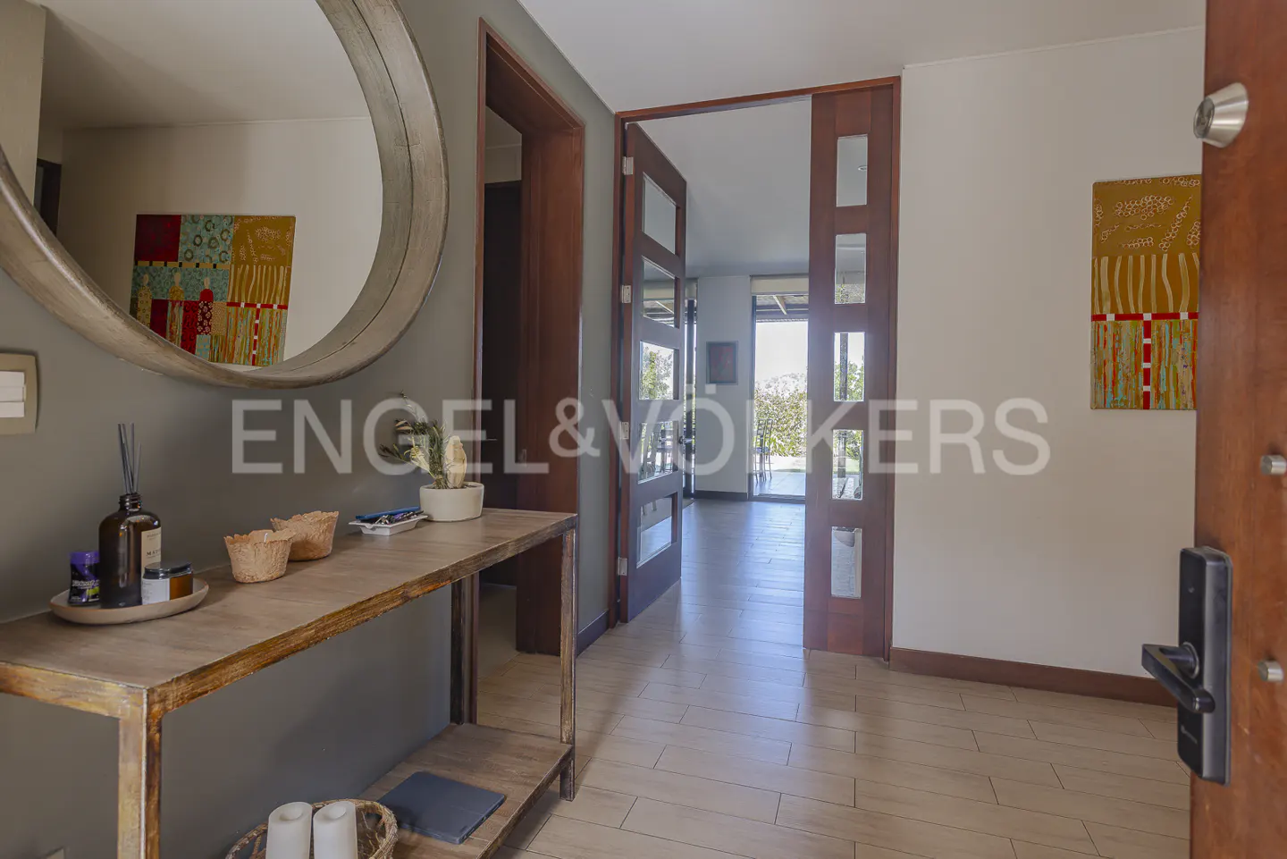 Entryway with a round mirror above a wooden console table, leading to an open doorway with a view of greenery.