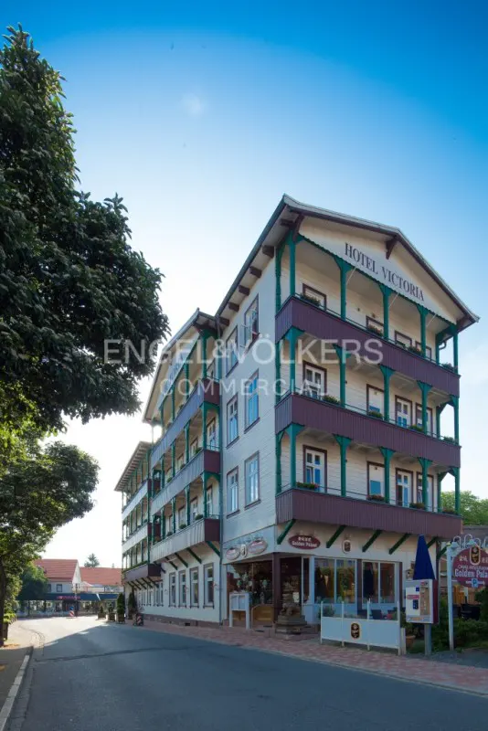 Exterior of Hotel Victoria, a white building with green trim and burgundy balconies, under a blue sky. Engel & Völkers logo visible.