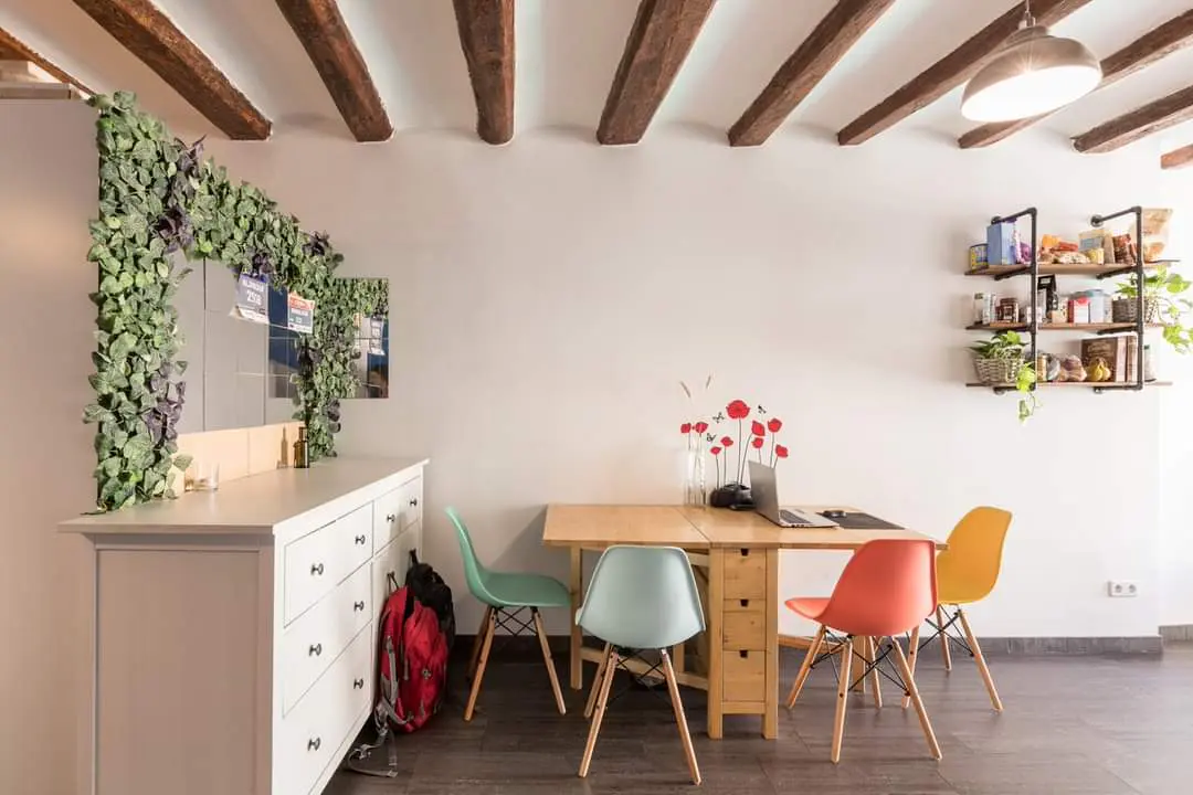 Interior view of a dining area with a wooden table, colorful chairs, and a white dresser with green foliage decor.