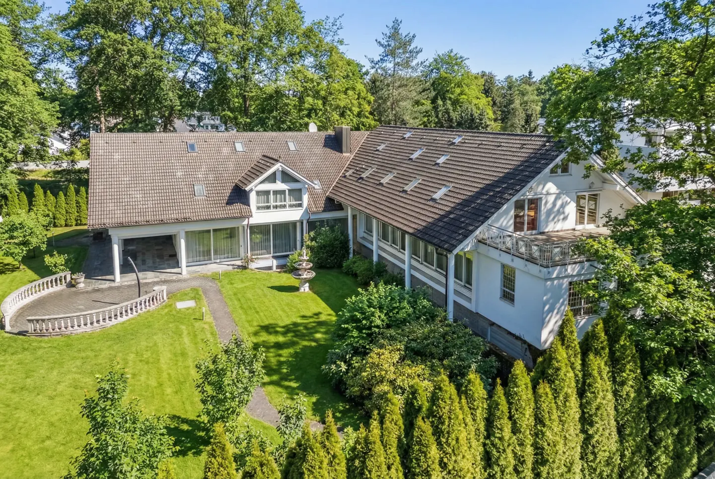 Aerial view of a white house with a brown roof, surrounded by green trees and a lawn.
